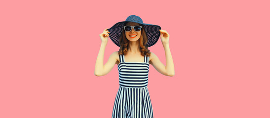 Summer portrait of beautiful young woman model wearing black round straw hat, striped dress on pink background