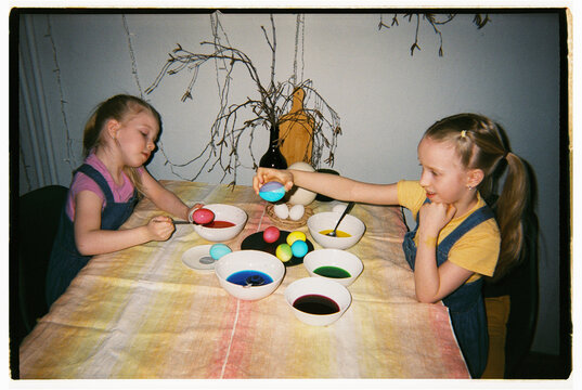 Two little girls paint eggs in deep plates