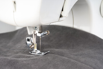 Modern sewing machine presser foot with gray fabric and thread, closeup. Sewing process clothes, curtains, upholstery. Business, hobby, handmade, zero waste, recycling, repair concept