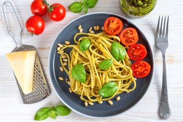 Pasta spaghetti with pesto sauce and fresh basil leaves in black bowl on white wooden background served with food ingredients. Traditional italian cuisine. Top view, flat lay