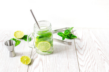 Fresh iced cold mojito lemonade summer drink, cocktail with sliced lime, bright green mint leaves and frozen ice cubes in a transparent cup, mason jar on wooden table
