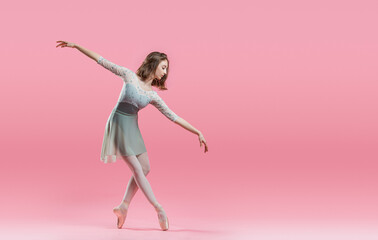 elegant young ballerina in pointe shoes dancing on a delicate pink background