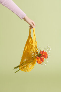 The hand holds a yellow bag with summer flowers on a light background