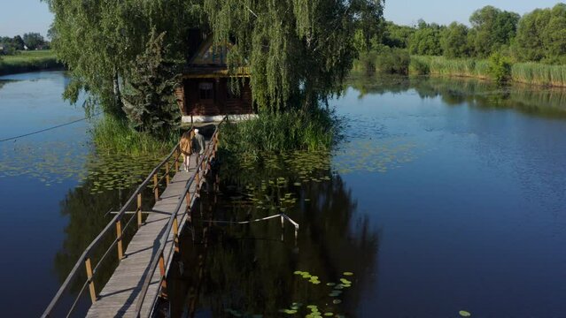 Old wooden fisherman's and hunter's house on the island. Landscape with couple in love holding hands walking on old wooden bridge to the cabin on lake. Old Solotvyn Village, Ukraine
