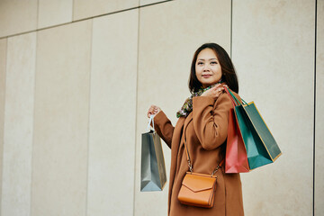Mid adult Asian woman with shopping bags looking at camera.