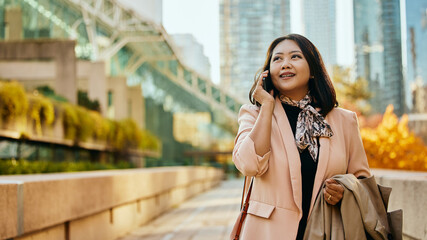 Fototapeta premium Asian businesswoman communicating on cell phone on city street.