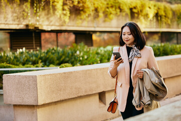 Asian female entrepreneur texting on mobile phone on street.