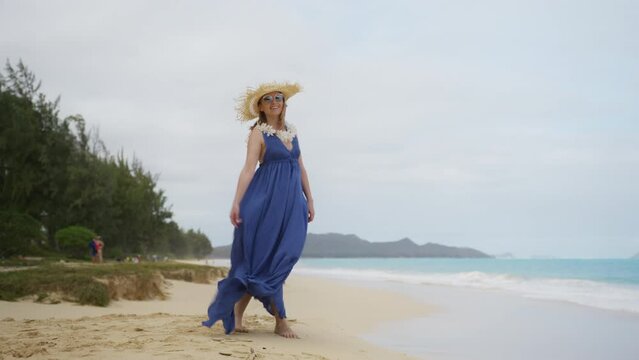 RED camera scenic shot of traveller lady with lei flower neckless walking with scenic Oahu nature. 30s authentic traveler woman in purple maxi boho style dress and straw hat enjoying Hawaiian beach 4K