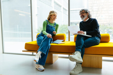 Coworkers discussing project sitting on yellow sofa in a workspace
