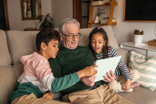 grandfather with his two grandchildren using ipad at home