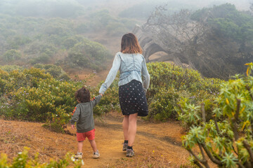 Fototapeta premium Mother and son walking with flowers to a Sabinar tree twisted by the wind of El Hierro. Canary Islands