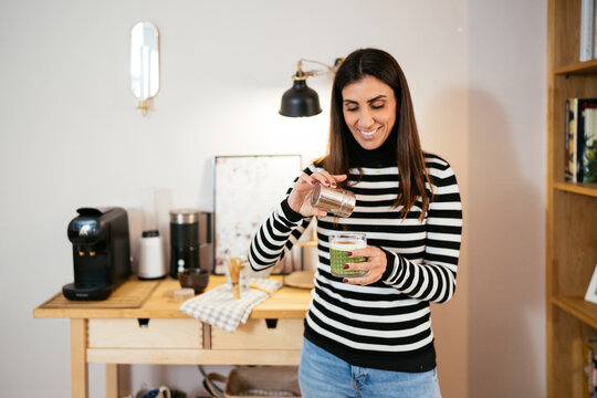 Smiling woman preparing matcha latte at home