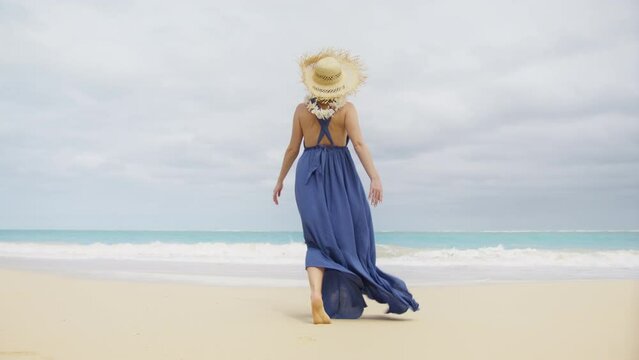 Happy girl in fashionable trendy boho style Summer vacation. Back view woman in romantic purple boho maxi dress flattering at sea breeze walking on tropical beach at beautiful ocean bokeh background