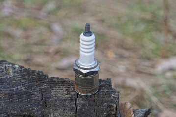 one small metal white gray spark plug stands on a table outside