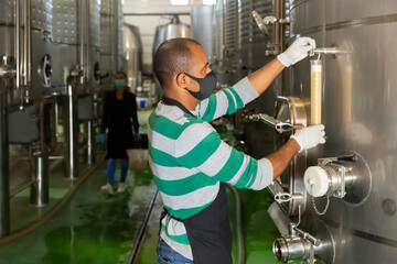 Winemaker in mask checking wine at fermentation department of winery, winemaking process