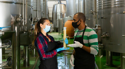 Man and a woman in protective masks analyze the white wine in a beaker