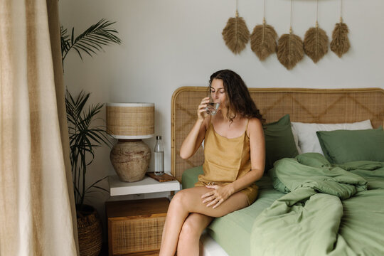 Portrait of a woman sitting on bed and drink glass of water