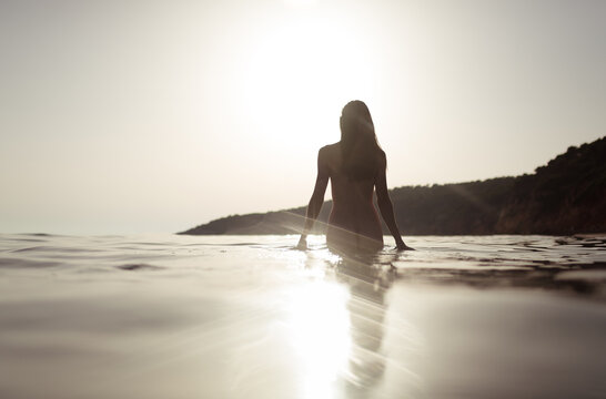 Woman walking in beach water towards the sun