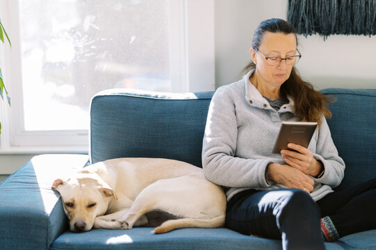 Middle aged woman relaxing on couch, reading e-book on a device