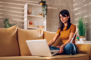 Woman using laptop while sitting on a yellow sofa at home