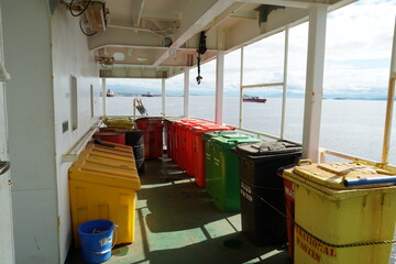 Plastic garbage bins of different colors and for various waste, firmly tight to the railings are situated in superstructure on the stern part of cargo container vessel sailing through Atlantic Ocean.
