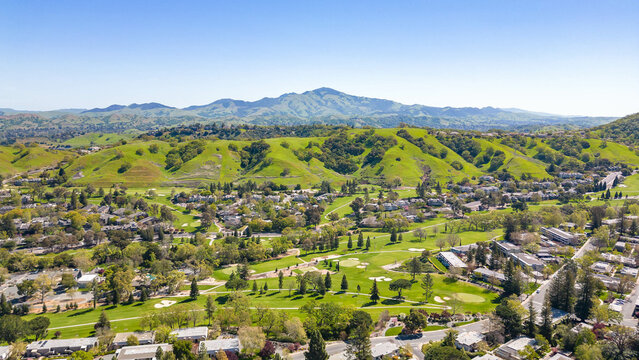 A stunning drone photo captures the Rossmoor community's picturesque beauty, showcasing homes, a golf course, green hills, and a clear blue sky.