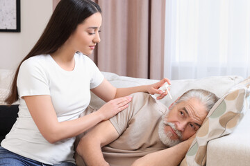 Young woman spraying medication into man's ear at home