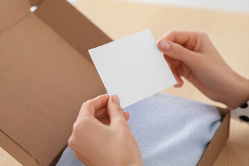 Woman holding greeting card near parcel with Christmas gift, closeup
