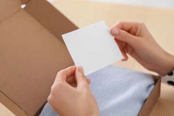 Fototapeta premium Woman holding greeting card near parcel with Christmas gift, closeup