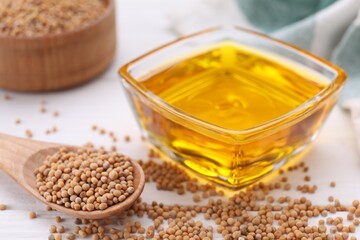 Bowl of natural oil and mustard seeds on white table, closeup