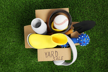 Phrase Yard Sale written on box with different stuff on green grass, top view