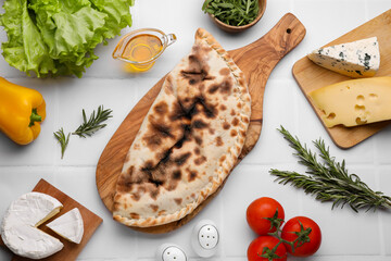 Tasty pizza calzone with cheese and different products on white tiled table, flat lay