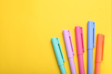 Many colorful markers on yellow background, flat lay. Space for text