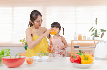 Asian children and her mom drink orange juice in the morning, they holding orange juice glass,...