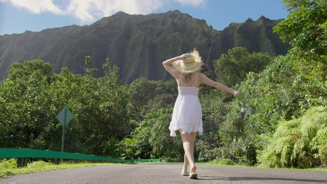 SLOW MOTION back view of beautiful sensual young woman in mini boho white dress and large straw hat walking in nature park on Oahu island, Hawaii. USA tourism on exotic tropical island USA travel shot