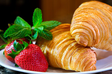 closeup of croissant sprinkled with powdered sugar with strawberries and mint leaves delicious dessert french breakfast restaurant serving cook at home decorate many different videos with strawberries