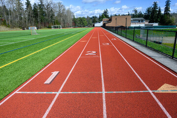 Four lane artificial sports track around an artificial turf soccer and football field, sunny spring...