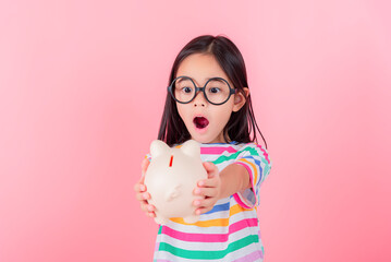 Little Asian girl saving money in a piggy bank, learning about saving, Kid save money for future education. Money, finances, insurance, and people concept