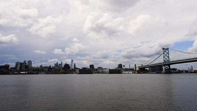 Philadelphia skyline over the calm Delaware River with the Benjamin Franklin Bridge on a cloudy warm day low and wide blue