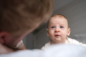 Cute two or three months baby boy looking at his parent or adult lying on belly on bed.Copy space.