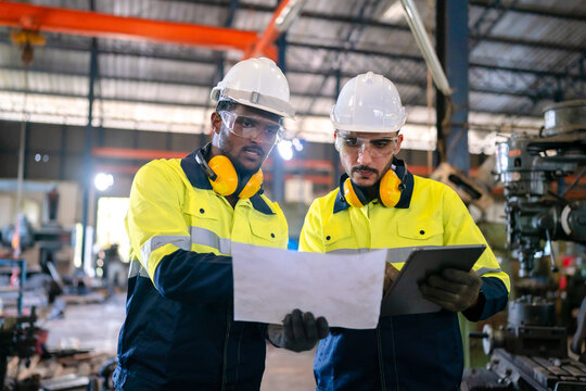 Production engineers in safety wear are assisting adjusting and maintaining CNC or factory machine, Male workers technician examining control the industrial tool, professional men at work in industry