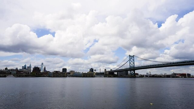 Dark Philadelphia skyline with clouds over the calm Delaware River with the Benjamin Franklin Bridge on a warm day low to water