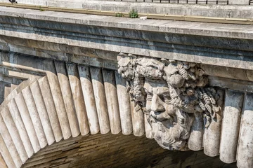 Photo sur Plexiglas Pont des Soupirs Stone faces on a historical bridge over the Seine River, in Paris, France.