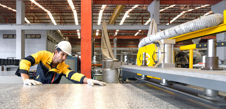 Young hispanic labor dressed in polyester jacket uniform, hardhat and protective glove insert PU Foam with Aluminium Foil Sheet in to metal sheet roofing machine.