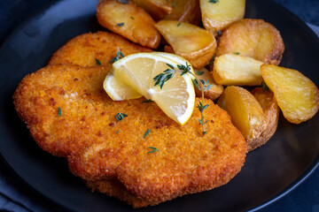 Chicken schnitzel with sauce, fried potatoes and lemon in a plate