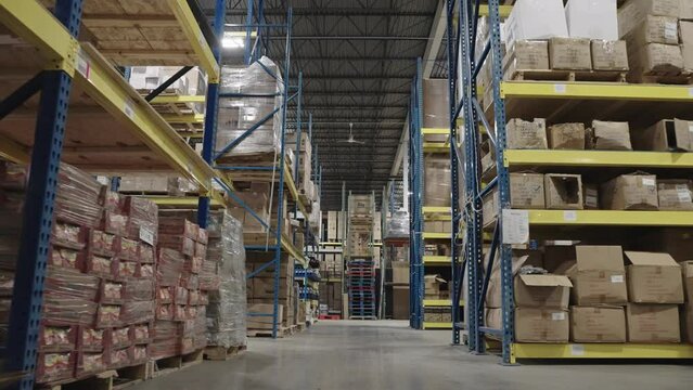 Big retail warehouse with cardboard boxes and packages on pallet rack shelves in a logistics center. Sorting and distribution facility for product delivery. Low to ground gimbal shot
