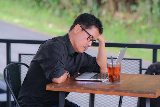 Sleepy Asian guy while working on his laptop at his home terrace