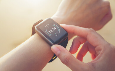 Woman hand wearing a smartwatch and checking active lifestyle and using fitness tracker outdoor on the beach.