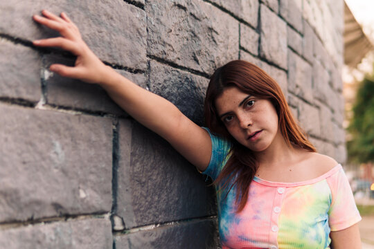 mujer joven adolescente posando en un muro de ladrillos  con ropa de colores urbana en la ciudad.