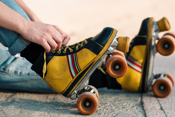 vista desde cerca de patines de cuatro ruedas de colores, con manos de mujer acomodando cordones.